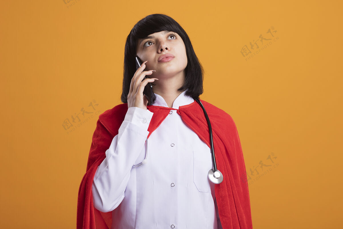 思考想着抬头看那个穿着医用长袍和斗篷的听诊器的年轻超级英雄女孩 她在橙色的墙上讲电话女孩穿电话