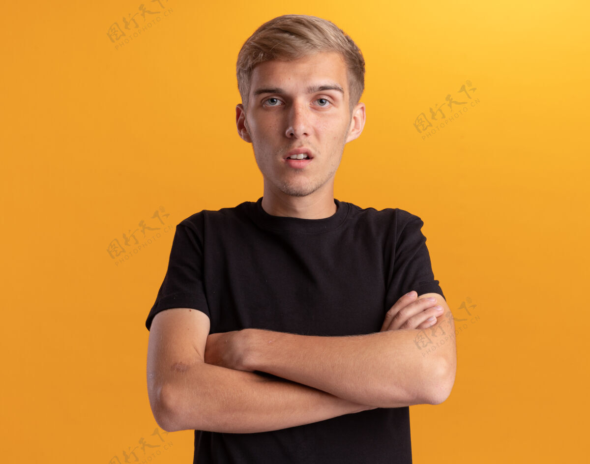困惑迷茫的年轻帅哥穿着黑衬衫双手交叉隔离在黄色的墙上穿帅哥手