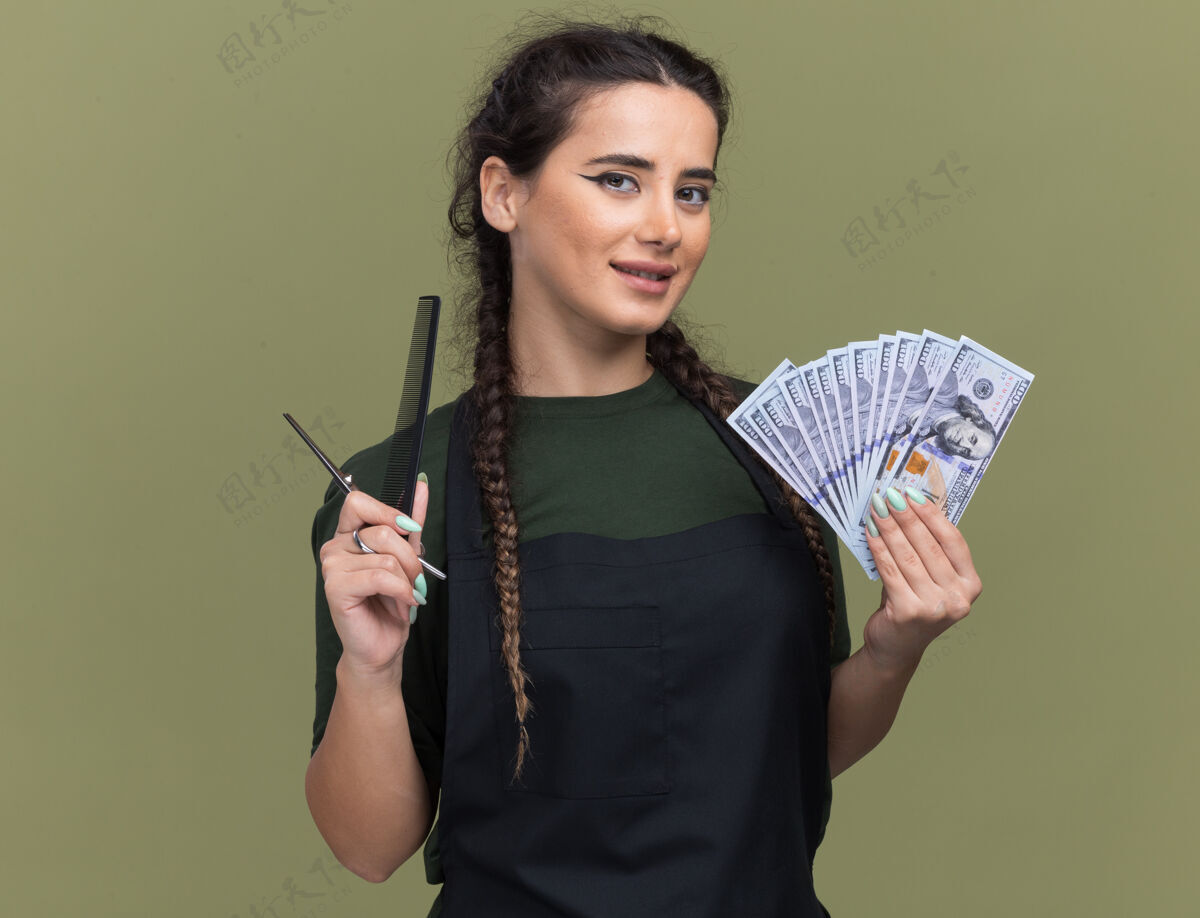 制服高兴的年轻女理发师穿着制服拿着现金与理发工具隔离在橄榄绿的墙上橄榄工具请拿着