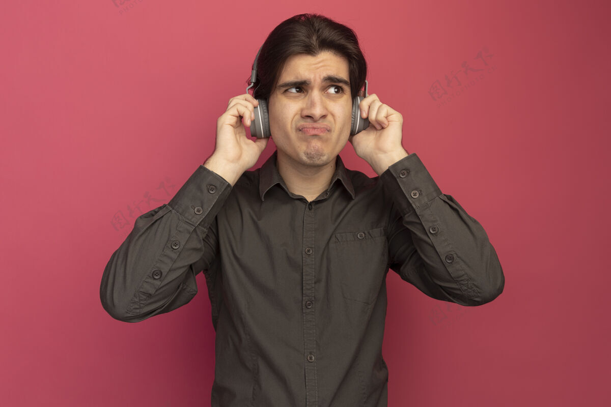 耳机一个穿着黑色t恤 戴着耳机的年轻帅哥站在粉红色的墙上 看起来很不自在戴着侧身小伙子