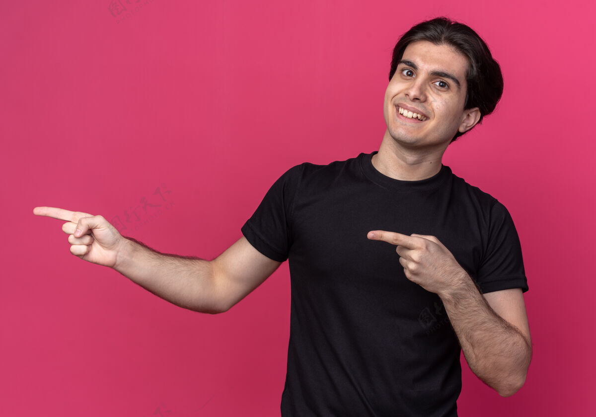 家伙面带微笑的年轻帅哥穿着黑色t恤点在侧面 隔离在粉红色的墙上 留有临摹空间帅气侧身穿