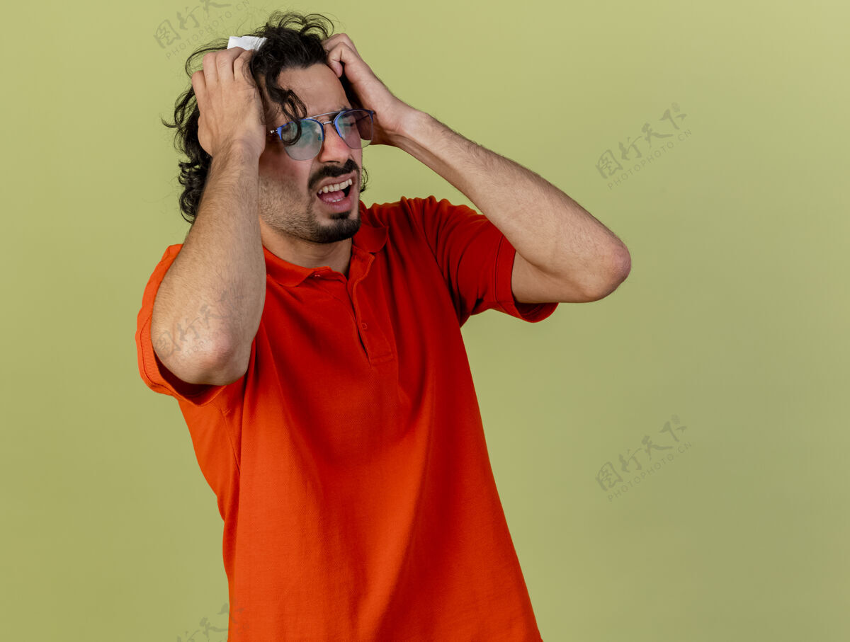 衣服紧张的年轻病人戴着眼镜拿着餐巾双手放在头上闭着眼睛隔离在橄榄绿的墙上有复印空间眼睛站着人