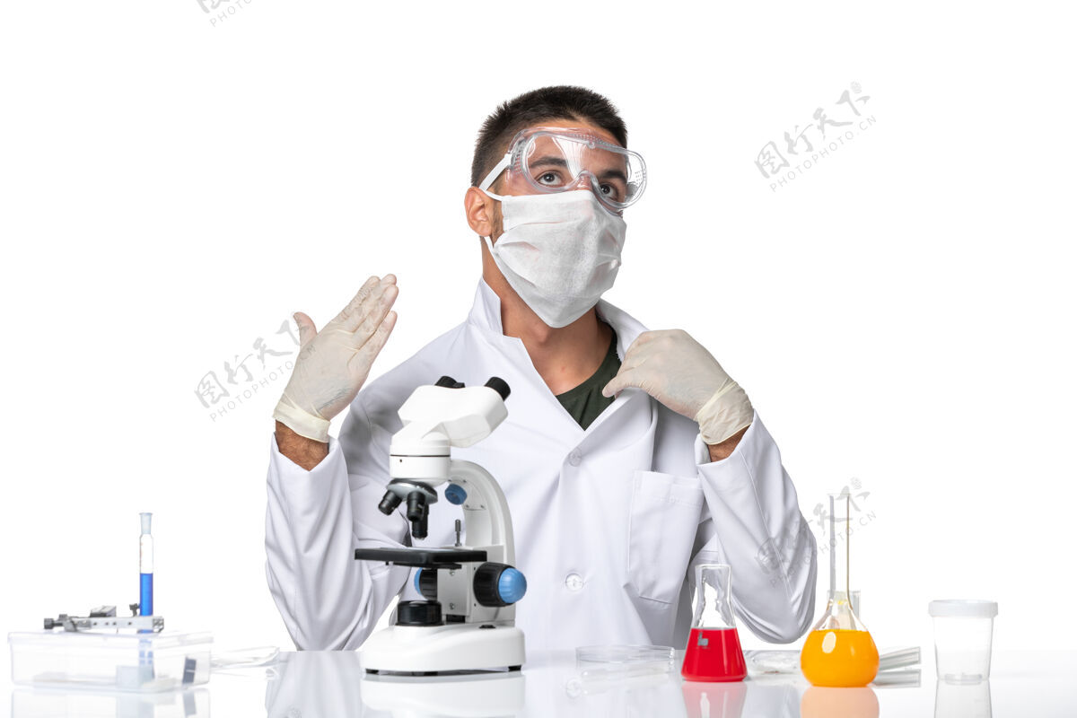 专业正面图：男医生穿着白色医疗服 戴着面罩 在一个浅白的空间里用显微镜观察显微镜光医学
