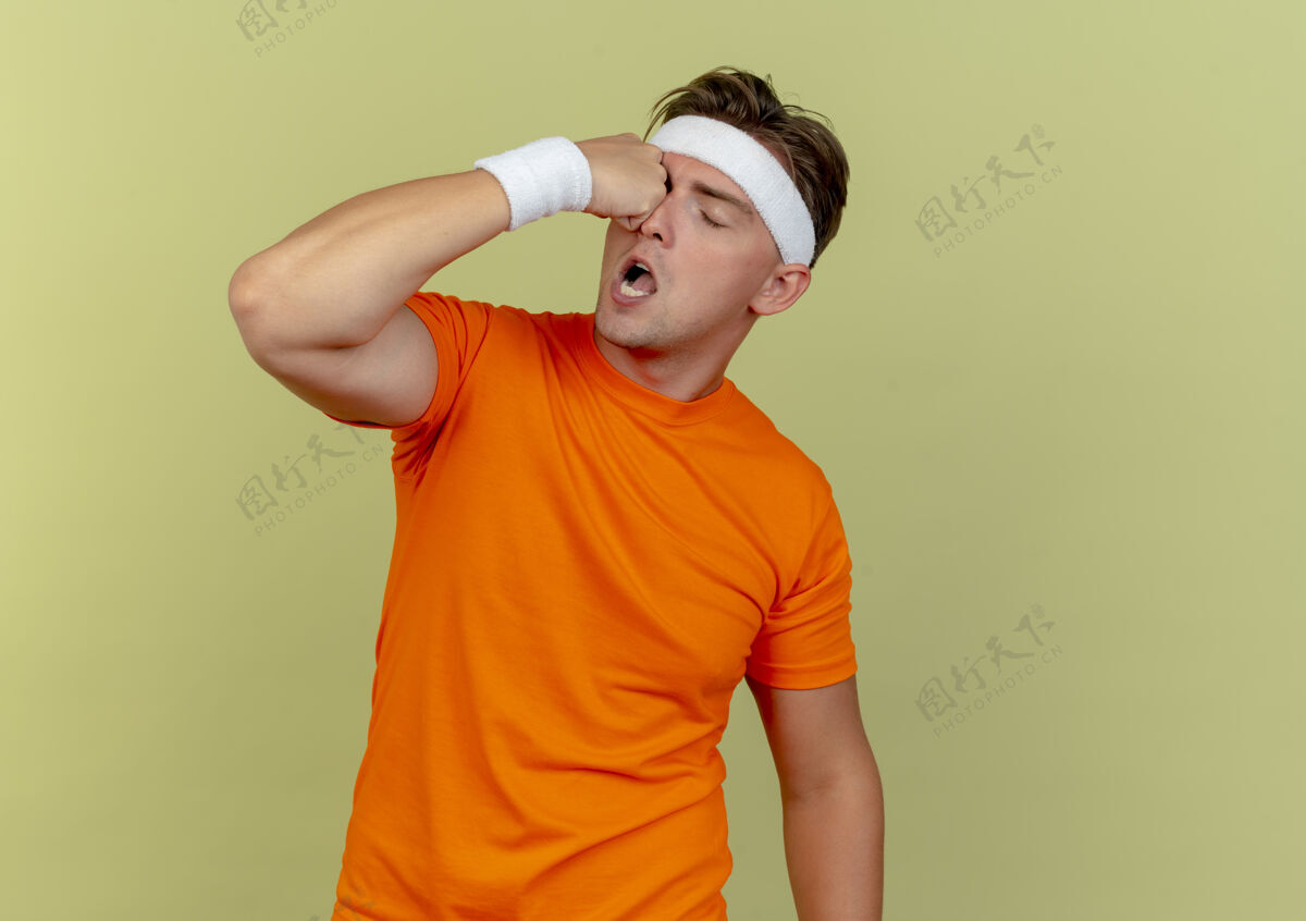 橄榄年轻英俊的运动型男子戴着头带和腕带踢自己的眼睛孤立在橄榄绿的背景与复制空间头带腕带穿