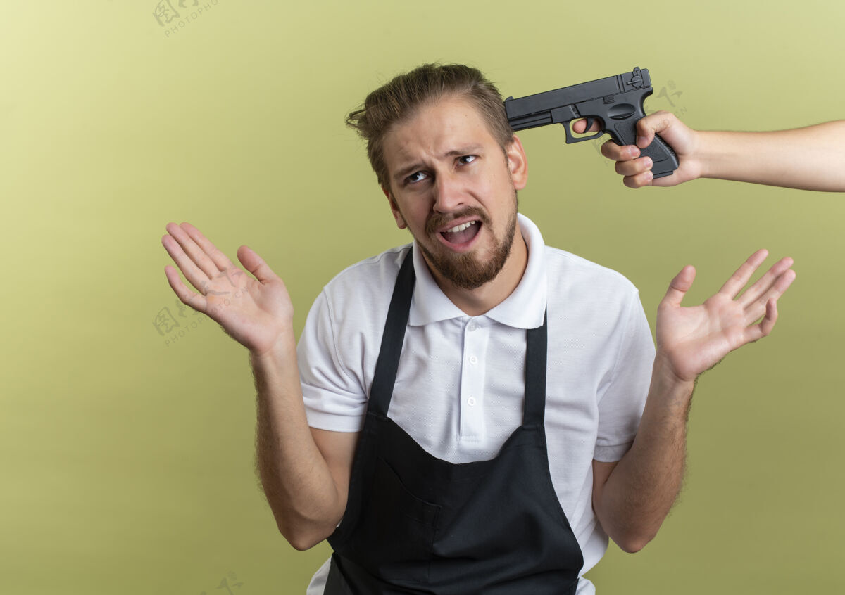 橄榄一个年轻英俊的理发师站在一旁 两手空空的 有人用枪指着他的头 背景是橄榄绿的头显示枪