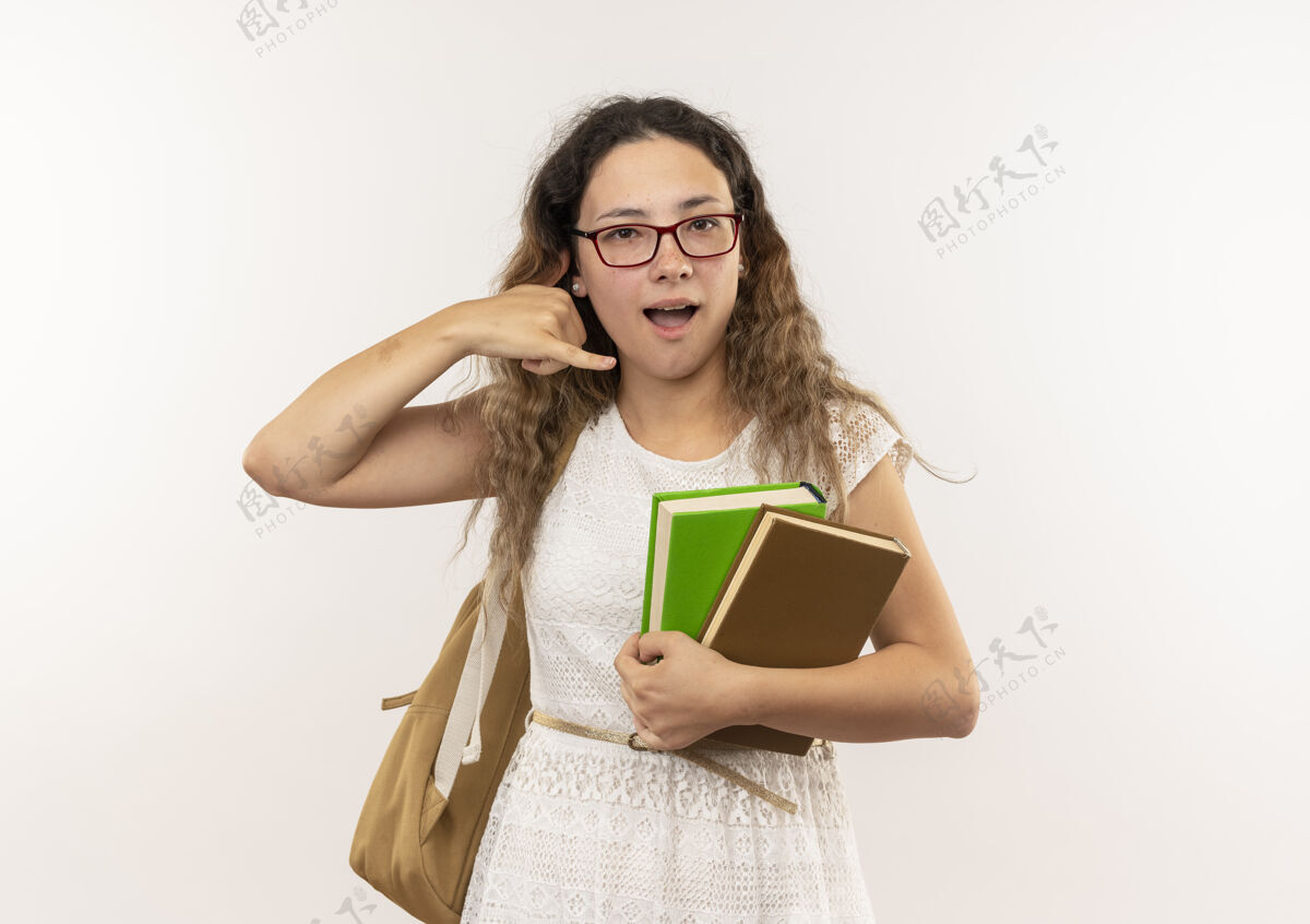 电话印象深刻的年轻漂亮的女学生戴着眼镜 背着书包在白色上做着孤立的呼唤手势手势印象眼镜