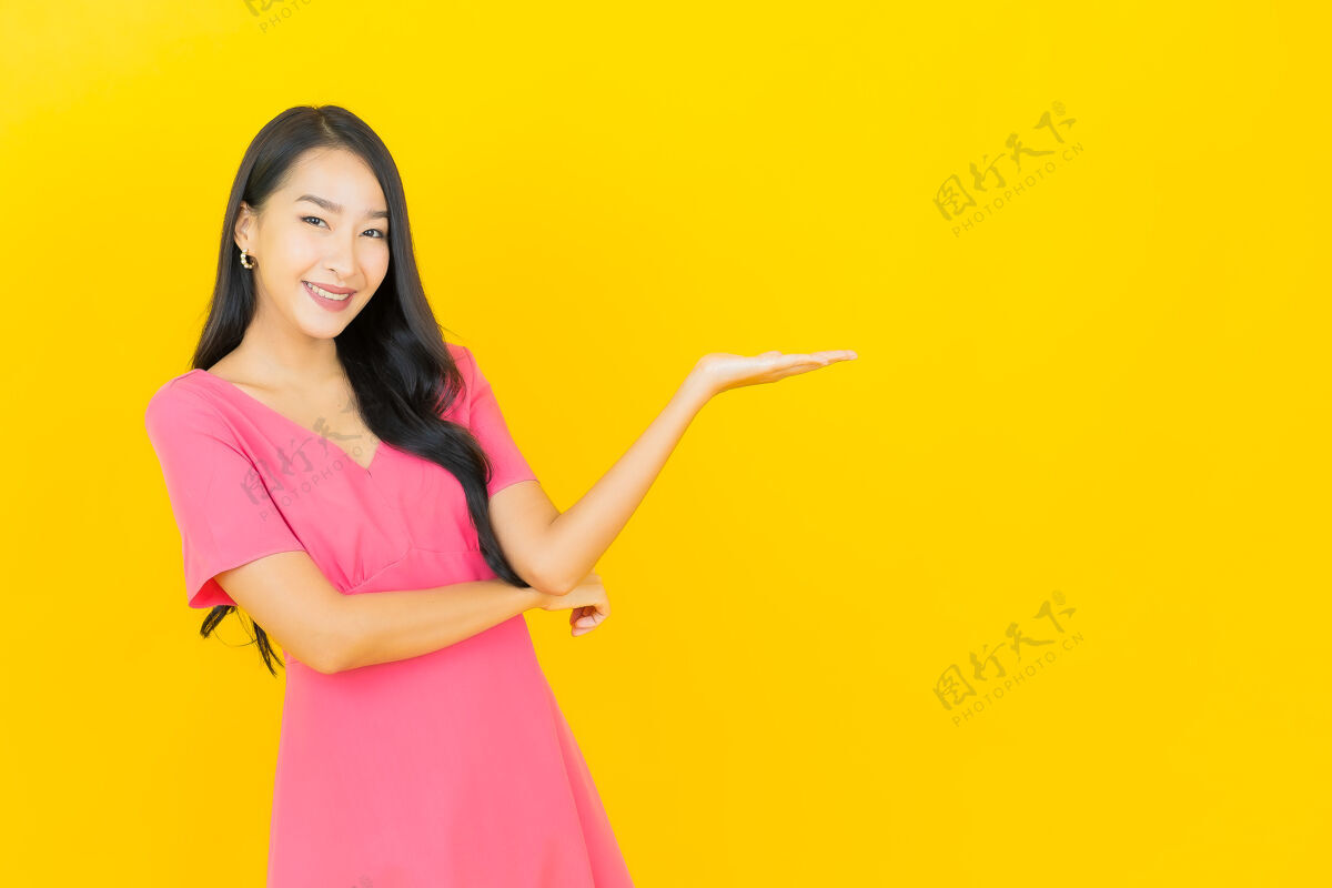 时髦黄色墙壁上 美丽的亚洲年轻女子身着粉色连衣裙微笑的画像微笑时尚肖像