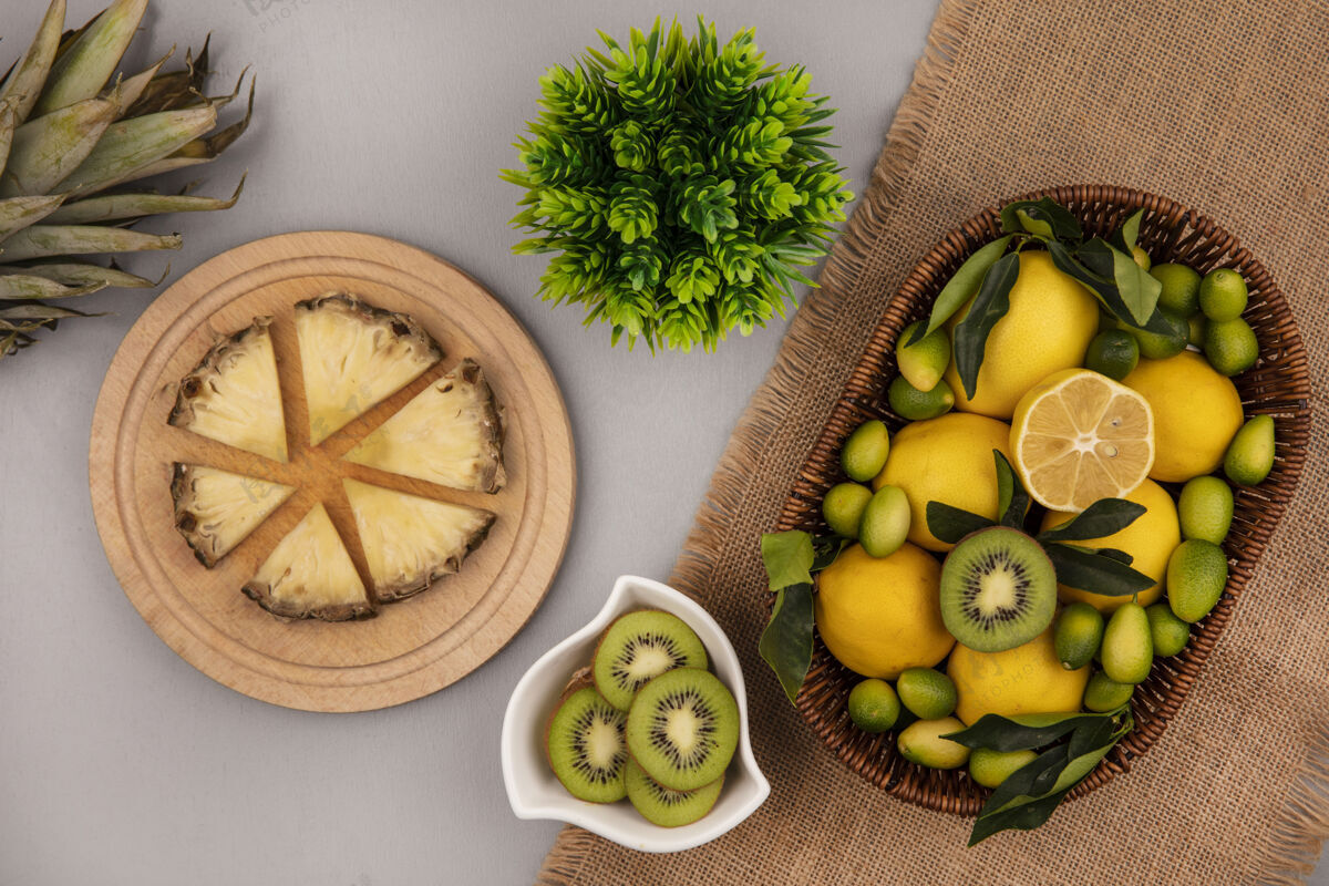 碗顶视图的水果 如猕猴桃金盏花和柠檬桶上的袋布与猕猴桃片碗上的菠萝片在木制厨房板上的灰色背景板猕猴桃水果