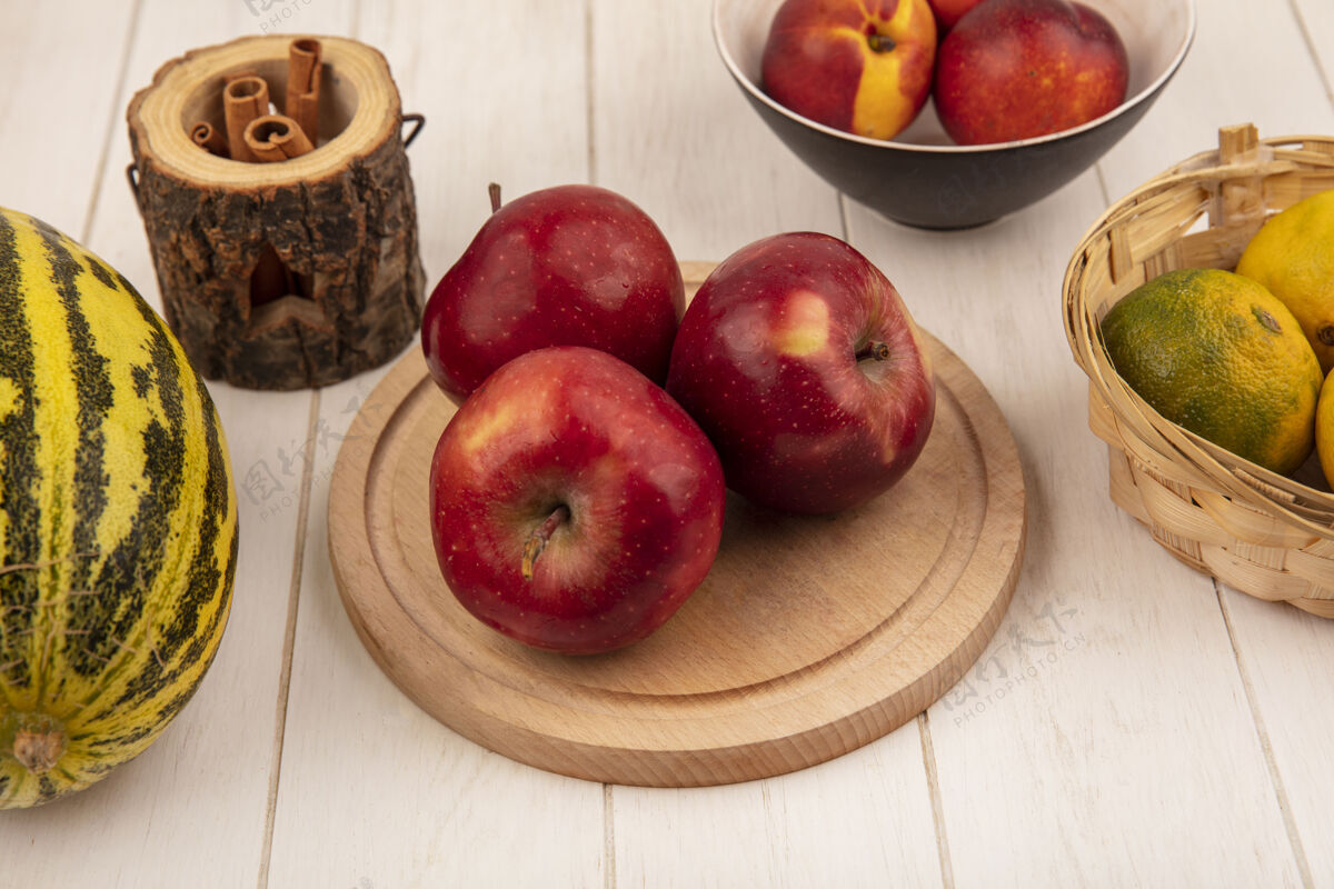 红色新鲜的红苹果在木制厨房板上的俯视图 哈密瓜和橘子放在白色木质背景的桶上白色视野木板