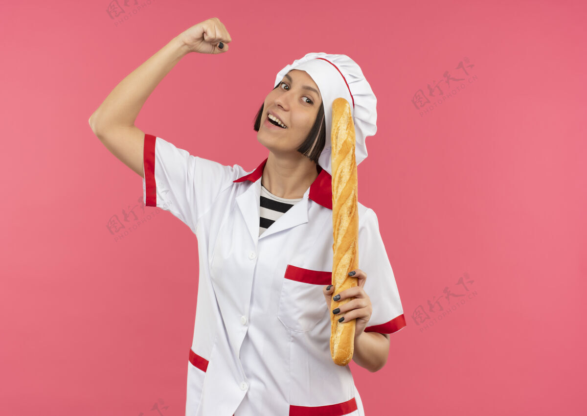粉红快乐的年轻女厨师身着厨师制服 拿着面包棒 在粉色上做着强烈的孤立的手势厨师年轻强壮