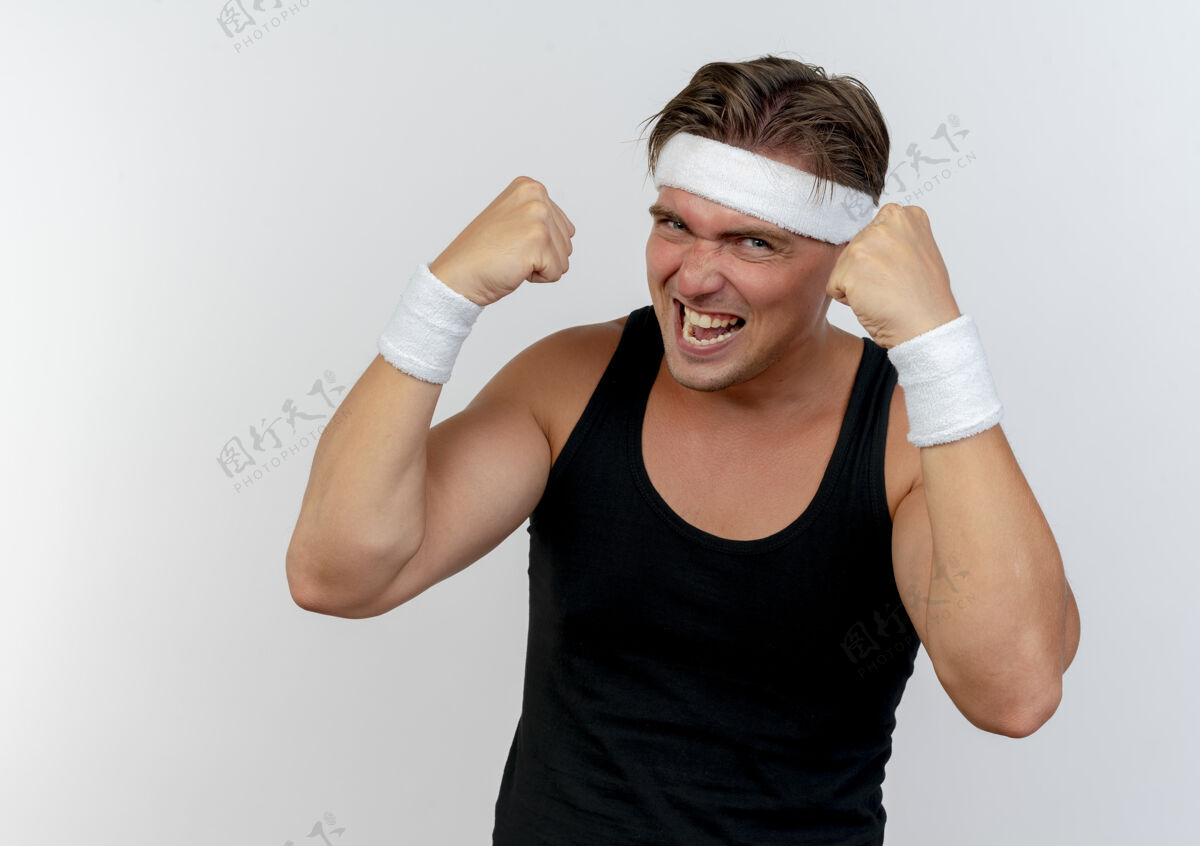拳头快乐的年轻英俊的运动男子戴着头带和手腕举起拳头孤立在白色头带腕带戴