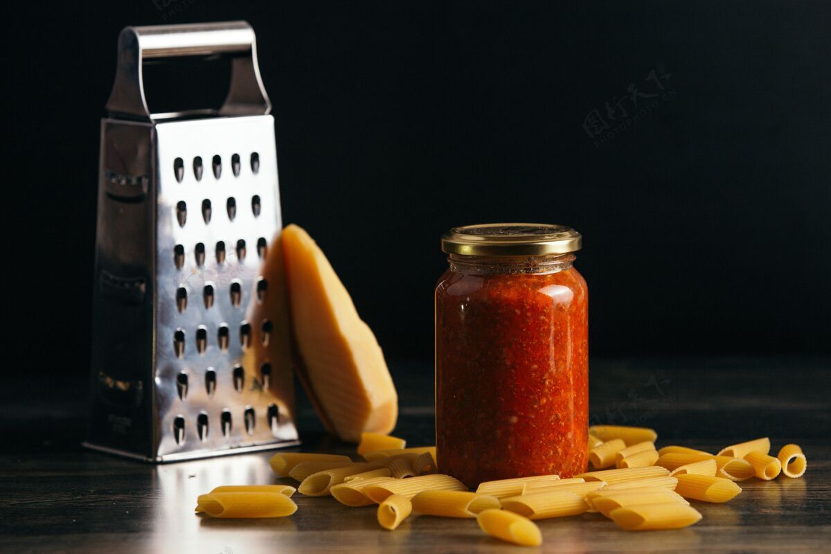背景特写潘恩意大利面和一罐酱汁放在桌子上 背景是奶酪和磨碎机美味晚餐红色