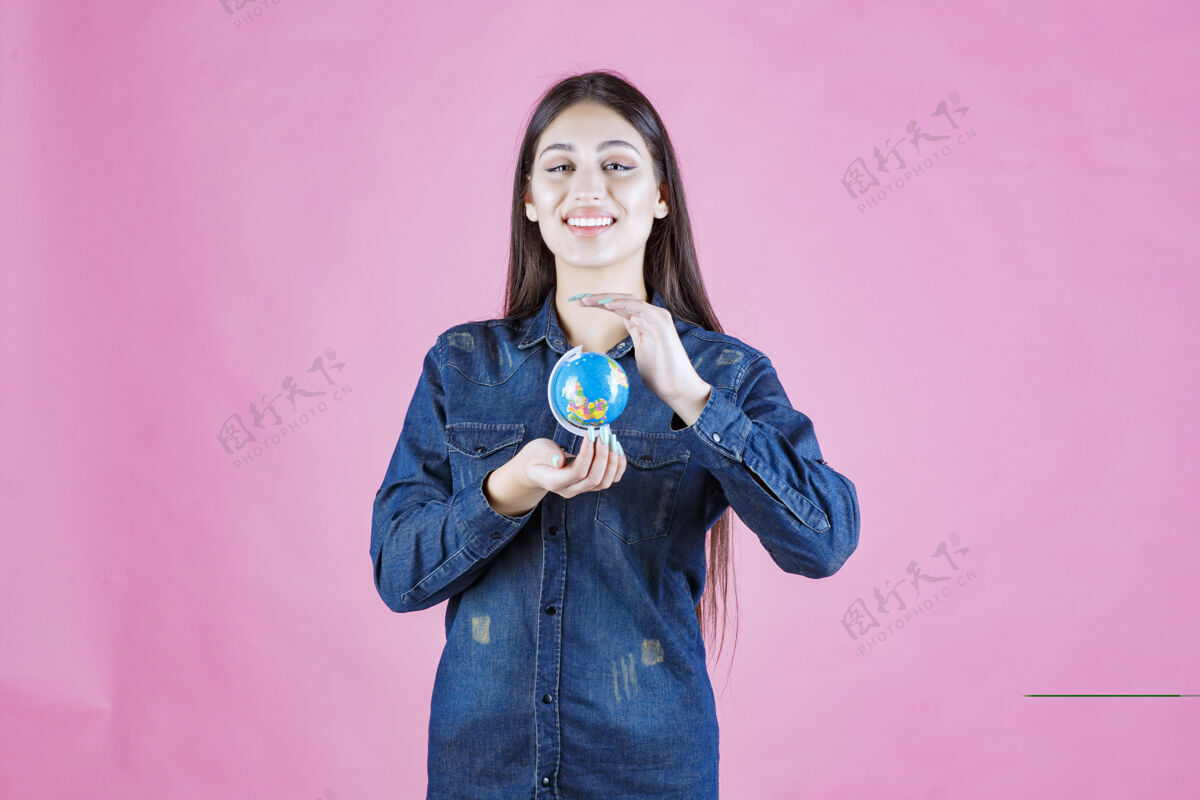 人穿着牛仔夹克的女孩双手捧着一个迷你地球仪学习装备成人