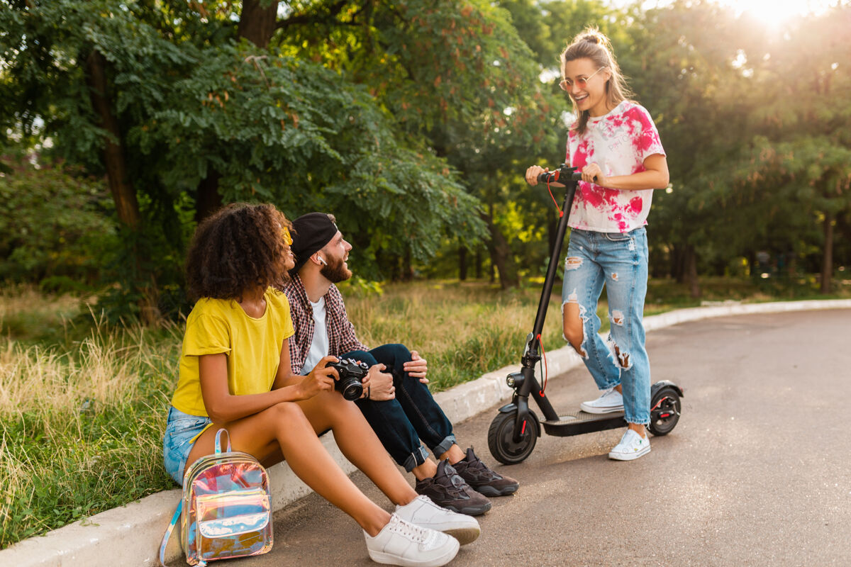 电力快乐的年轻朋友们坐在公园的草地上 带着电动脚踏车微笑着 男女同乐摩托车积极埃斯库特