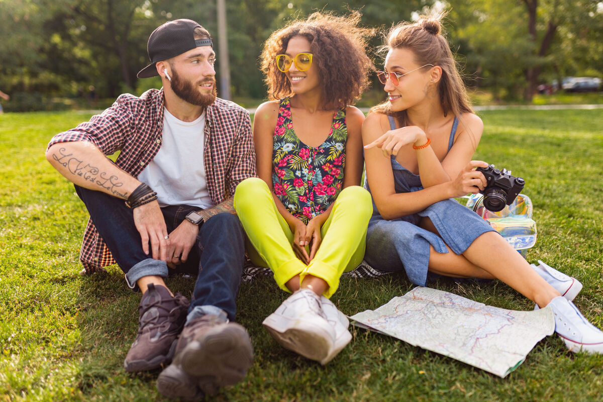 黄色快乐的年轻朋友陪伴坐在公园里 男女同乐 缤纷的夏日潮人时尚风格 带着相机旅行 谈笑风生年轻多种族多彩