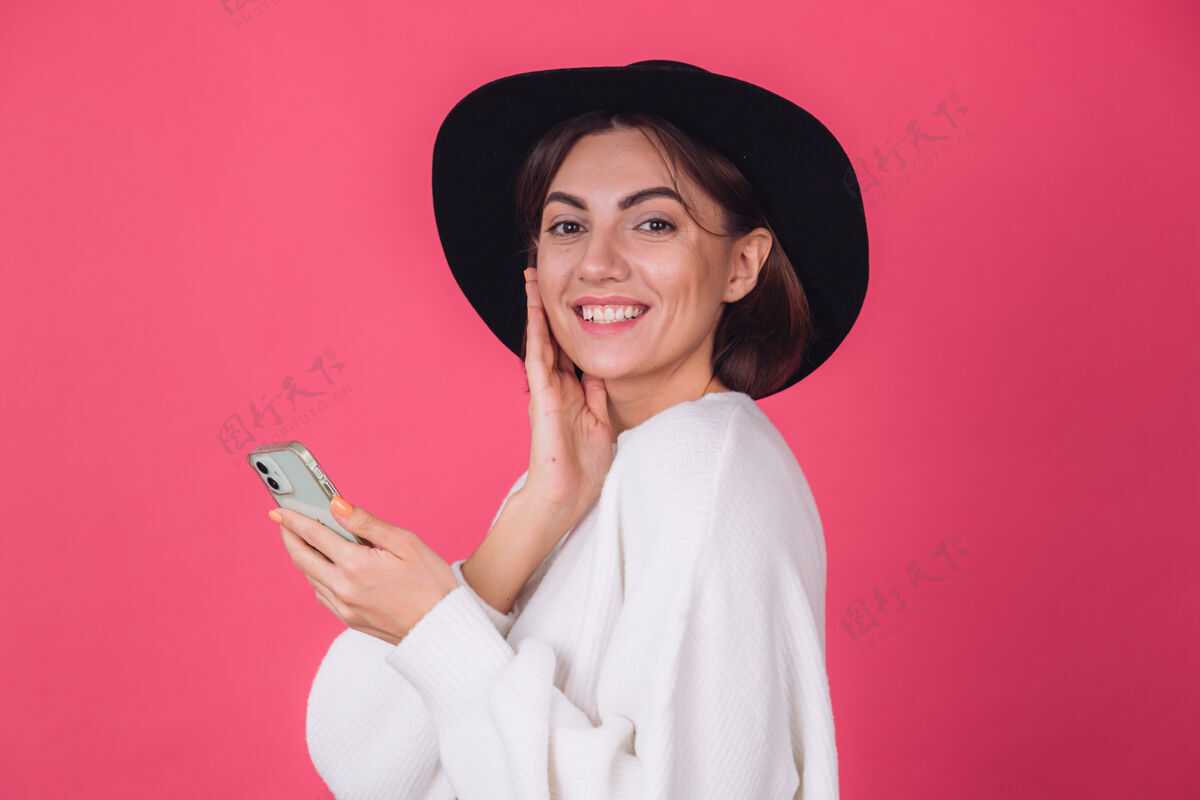 电话穿着白色休闲毛衣 戴着红粉色帽子的时髦女人欣喜若狂快乐年轻