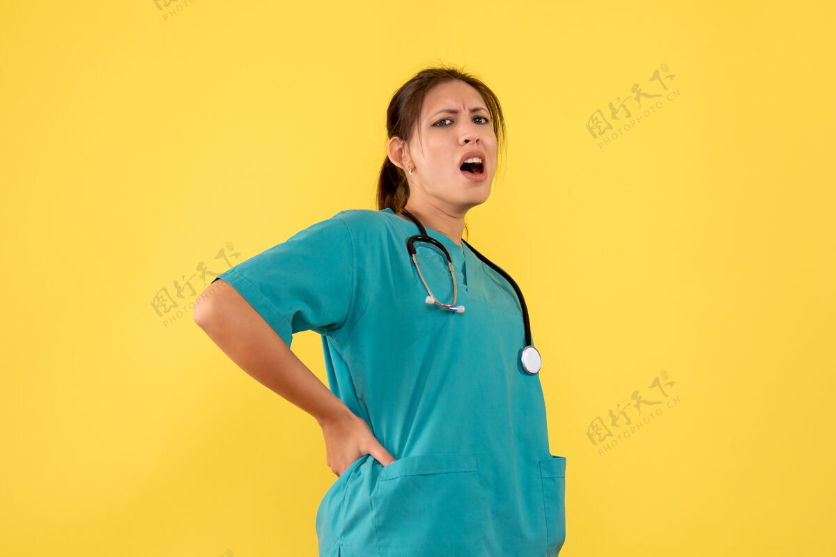 视图正面图黄色背景上穿着医用衬衫的女医生有点痛听诊器医疗黄色