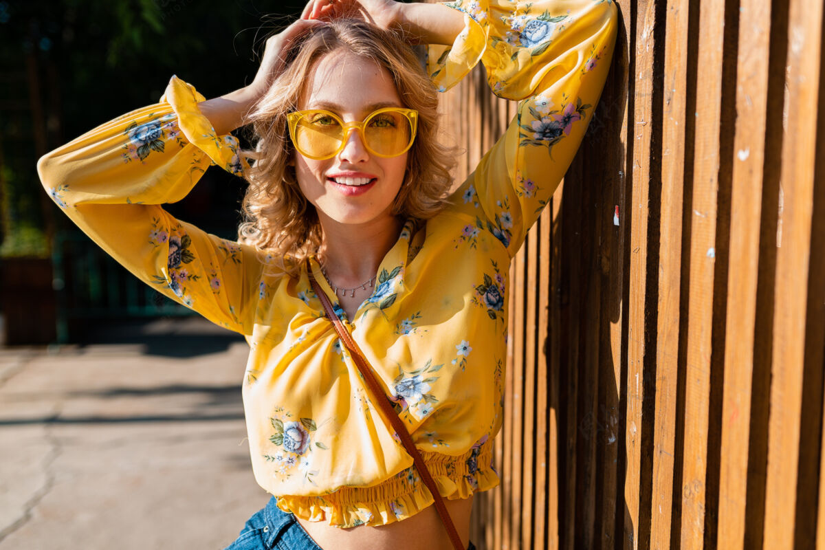 肖像美丽的金发时尚微笑的女人穿着黄色衬衫戴着太阳镜的肖像欢呼优雅街头