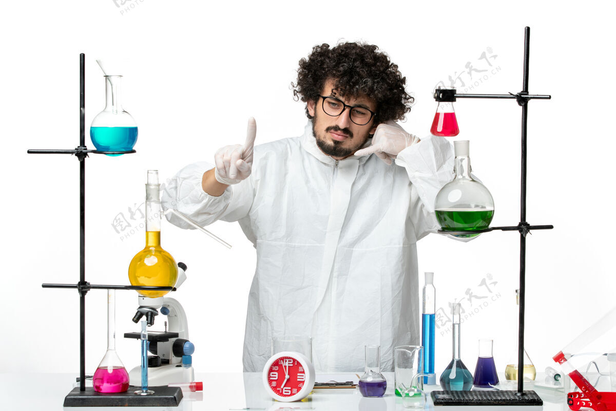 研究正面图身穿白色特殊套装的年轻男性科学家站在桌子旁 拿着解决方案化学套装烧杯