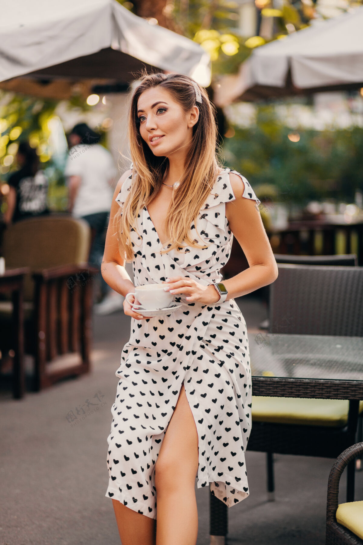 衣服美丽的微笑的女人穿着时尚的白色印花连衣裙坐在街上的咖啡馆里喝着一杯卡布奇诺春天餐厅人