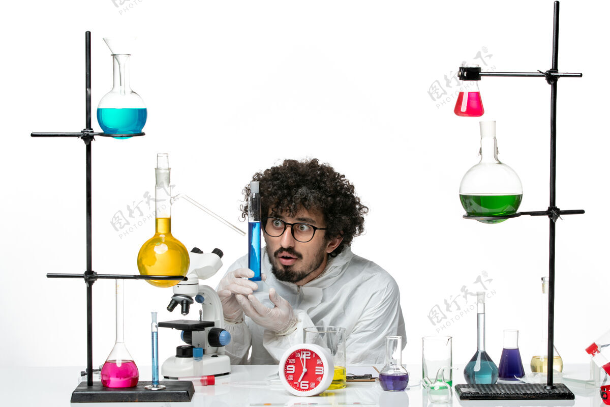 解决方案正面图：身着特殊套装的年轻男性科学家 在白墙上拿着装有溶液的烧瓶烧瓶生物学化学