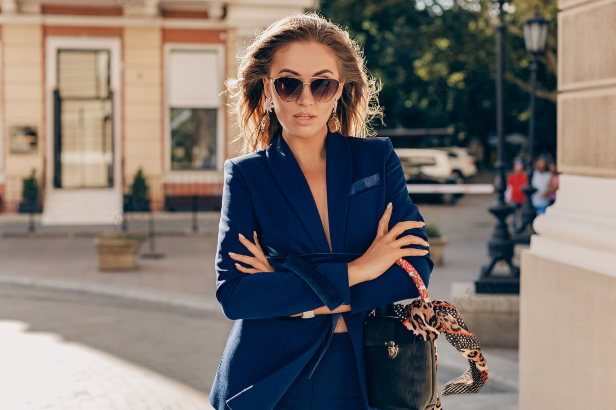 包优雅迷人的女人穿着蓝色时尚西装 戴着墨镜 手拿手袋走在街上春天城市优雅