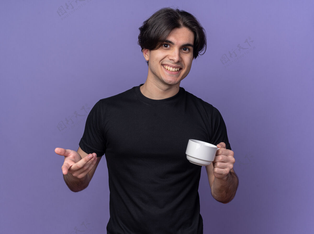 咖啡微笑着的年轻帅哥身穿黑色t恤 端着一杯咖啡 在紫色的墙上展示着你与世隔绝的姿态年轻抱着表演