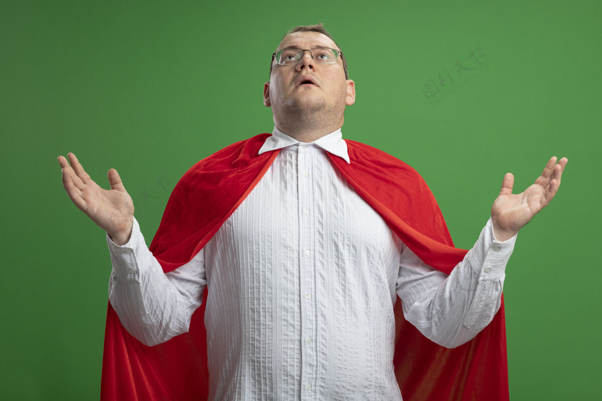 手令人印象深刻的成年斯拉夫超级英雄男子穿着红色斗篷 戴着眼镜 两手空空的 在绿色背景上孤立地抬头看印象绿色眼镜