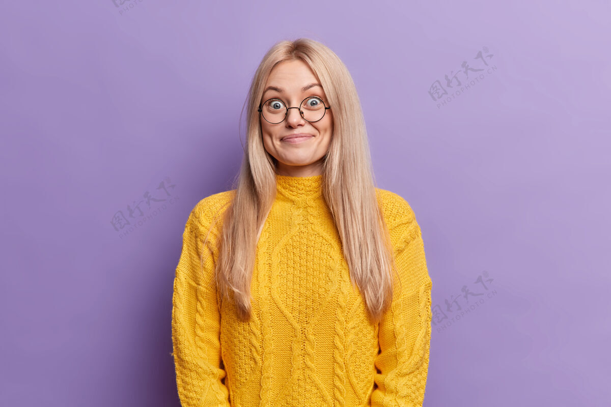 心情惊讶的金发欧洲女人有着欢快的表情戴着圆眼镜穿着黄色毛衣听到意想不到的喜讯室内人站着