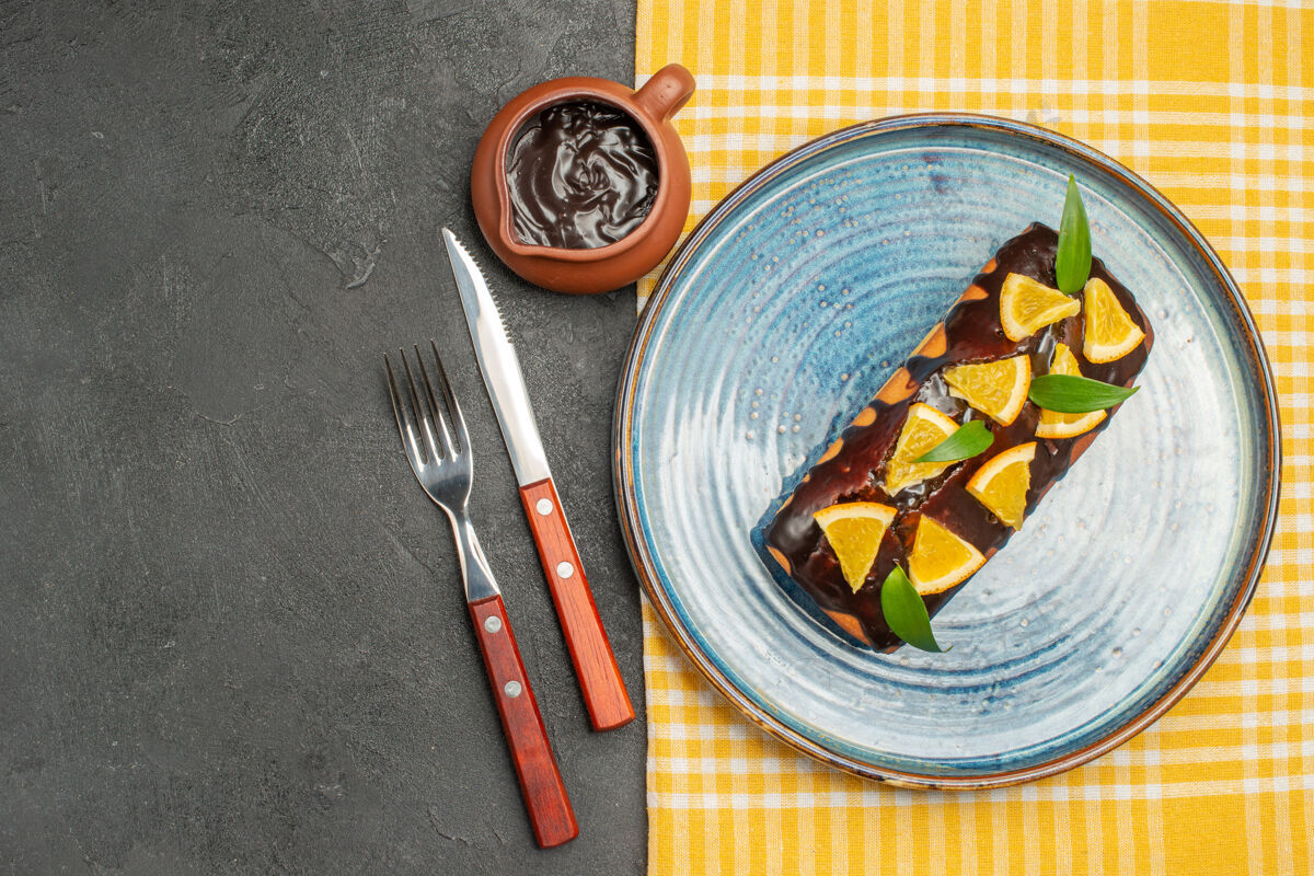深色用橘子和巧克力装饰的美味蛋糕 用叉子和刀子放在黑桌子上服务厨具特纳