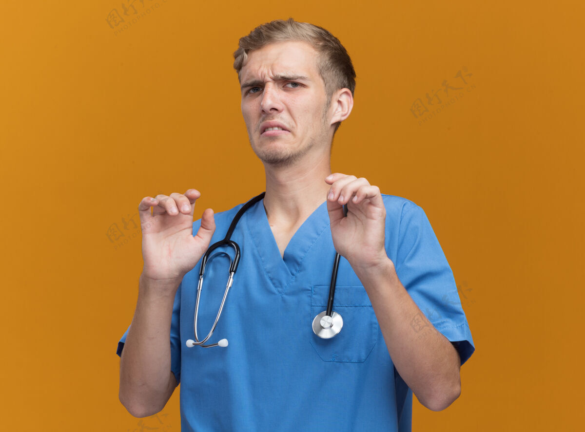年轻被吓坏了的年轻男医生穿着医生制服 听诊器被隔离在橙色的墙上医生制服害怕