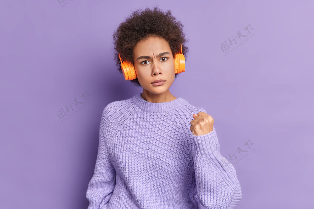紫色恼怒的卷发女子露出拳头 表达愤怒 用无线耳机听音乐暴力绝望女人