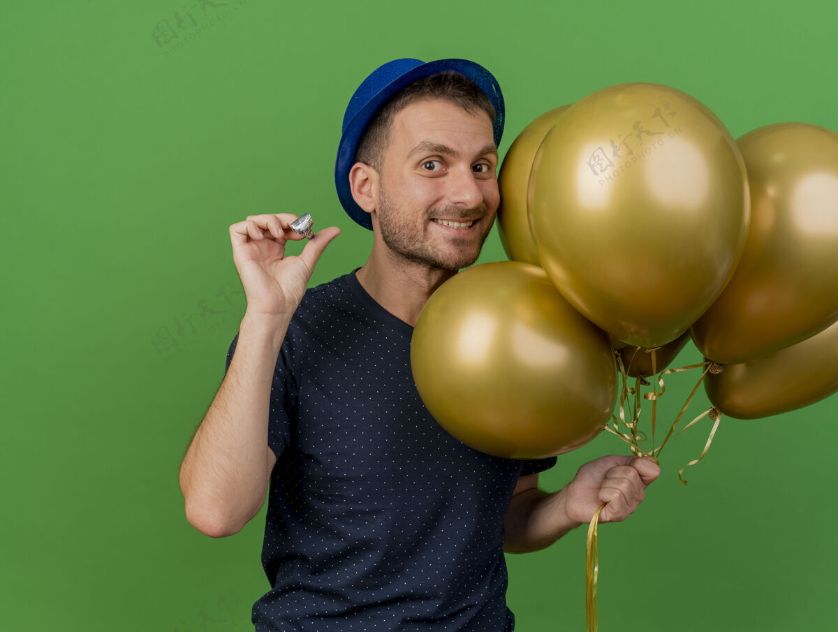 气球微笑英俊的白人男子戴着蓝色的党帽举行氦气球和党哨子隔离在绿色背景与复制空间哨子微笑聚会