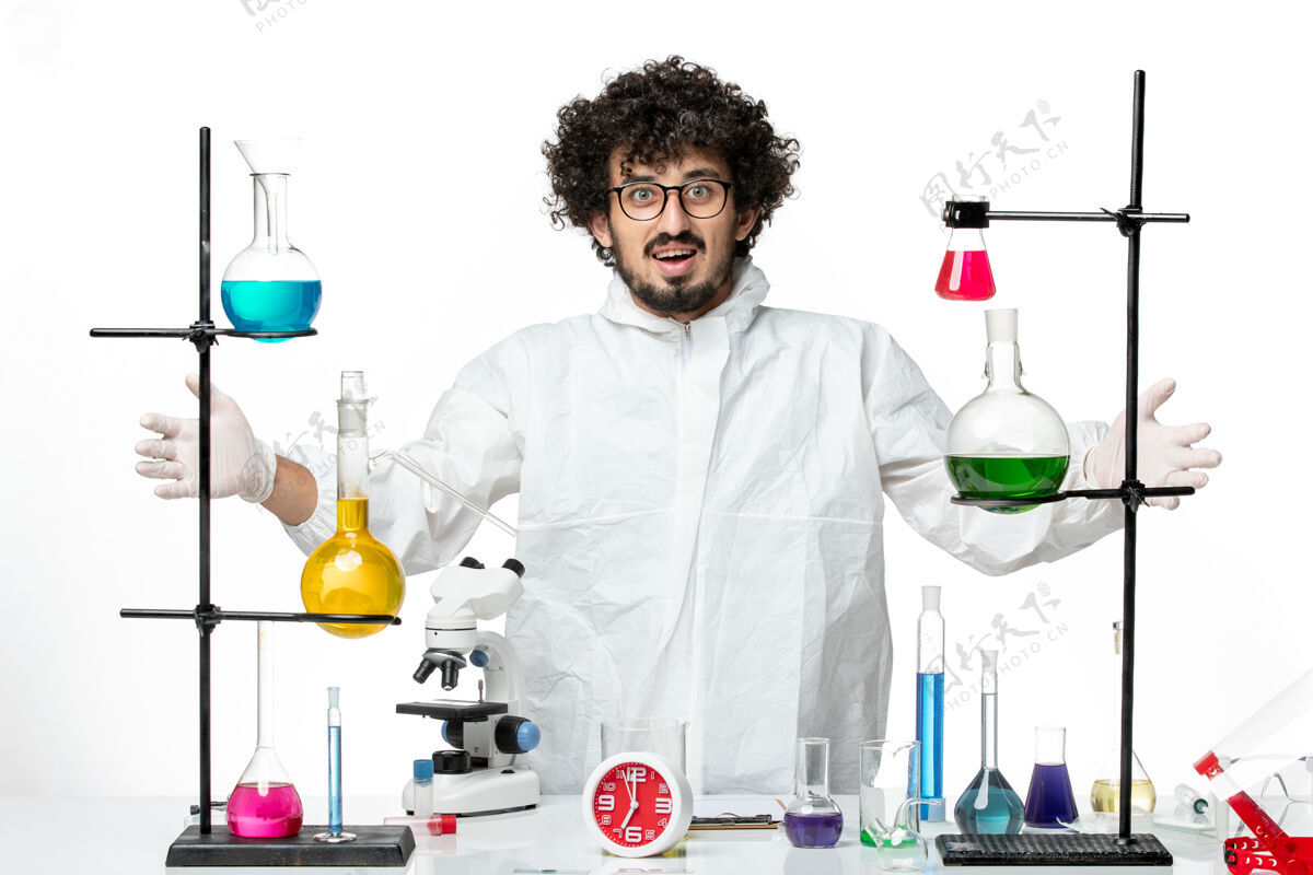 实验室正面图身着特殊套装的年轻男性科学家站在桌子周围 白色墙壁上有解决方案实验室化学烧杯