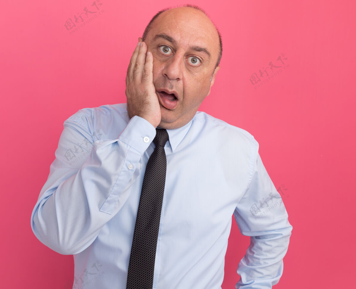 男人惊讶的中年男子穿着白色t恤 打着领带 手放在脸颊上 隔离在粉红色的墙上穿着领带T恤