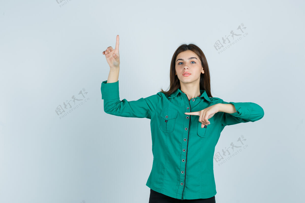 休闲年轻女孩用食指指着左上角 穿着绿色上衣 黑色裤子 表情严肃正视图女士自然衬衫