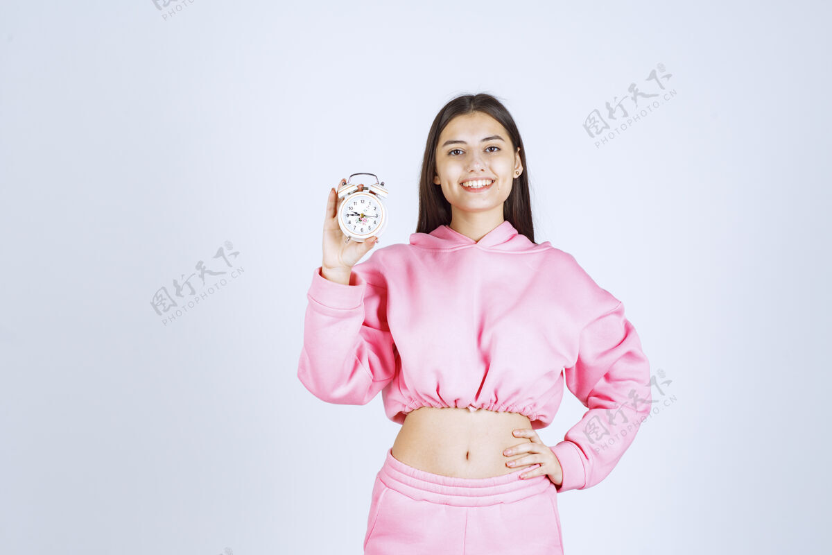 人类一个穿着粉色睡衣的女孩拿着一个闹钟 把它当作一个产品来推销模特方便服装