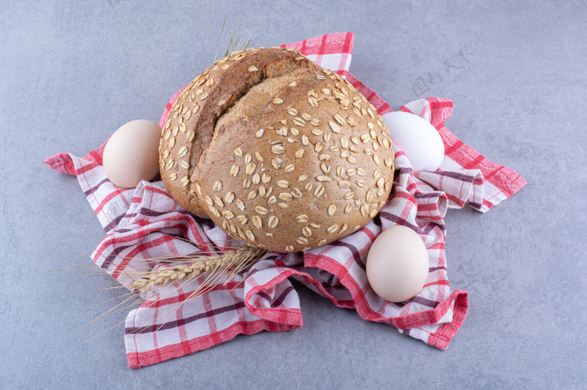 面包屑把麦秆 鸡蛋和一条面包放在大理石表面的毛巾上鸡蛋配料烘焙食品