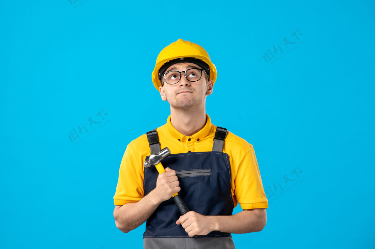 锤子前视图思考男建设者制服与锤子上的蓝色建筑工人表面帽子