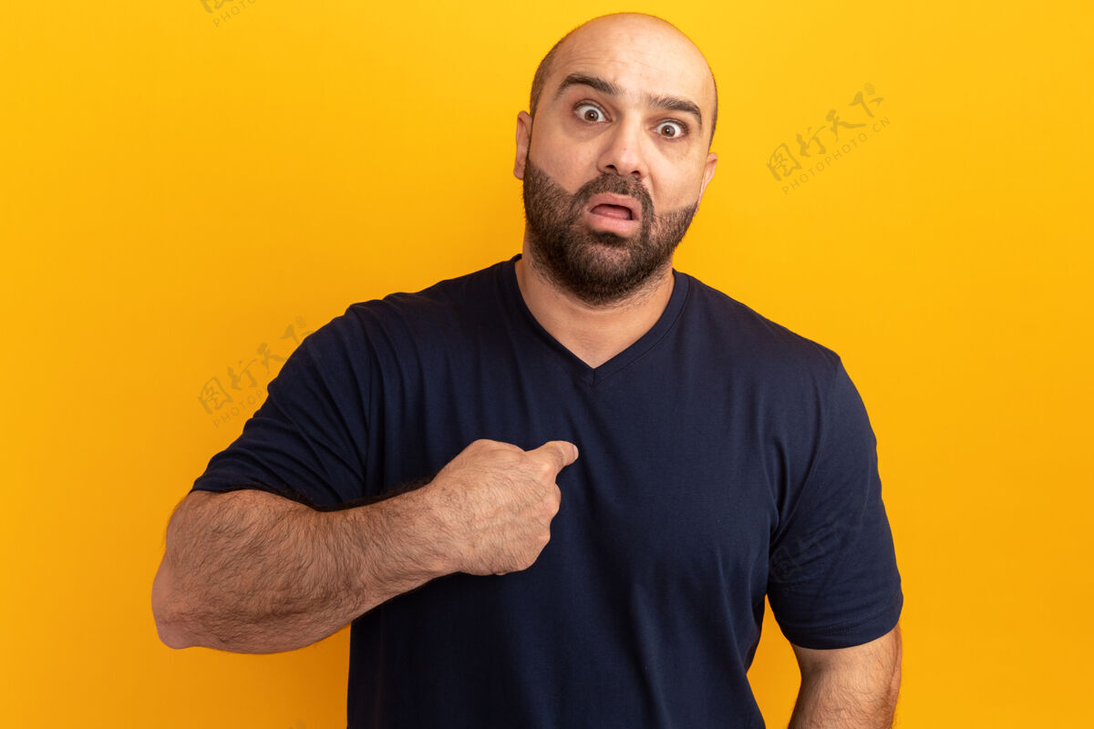 担心一个穿着海军t恤的大胡子男人担心又惊讶地用食指指着站在橙色墙上的自己惊讶站着目录