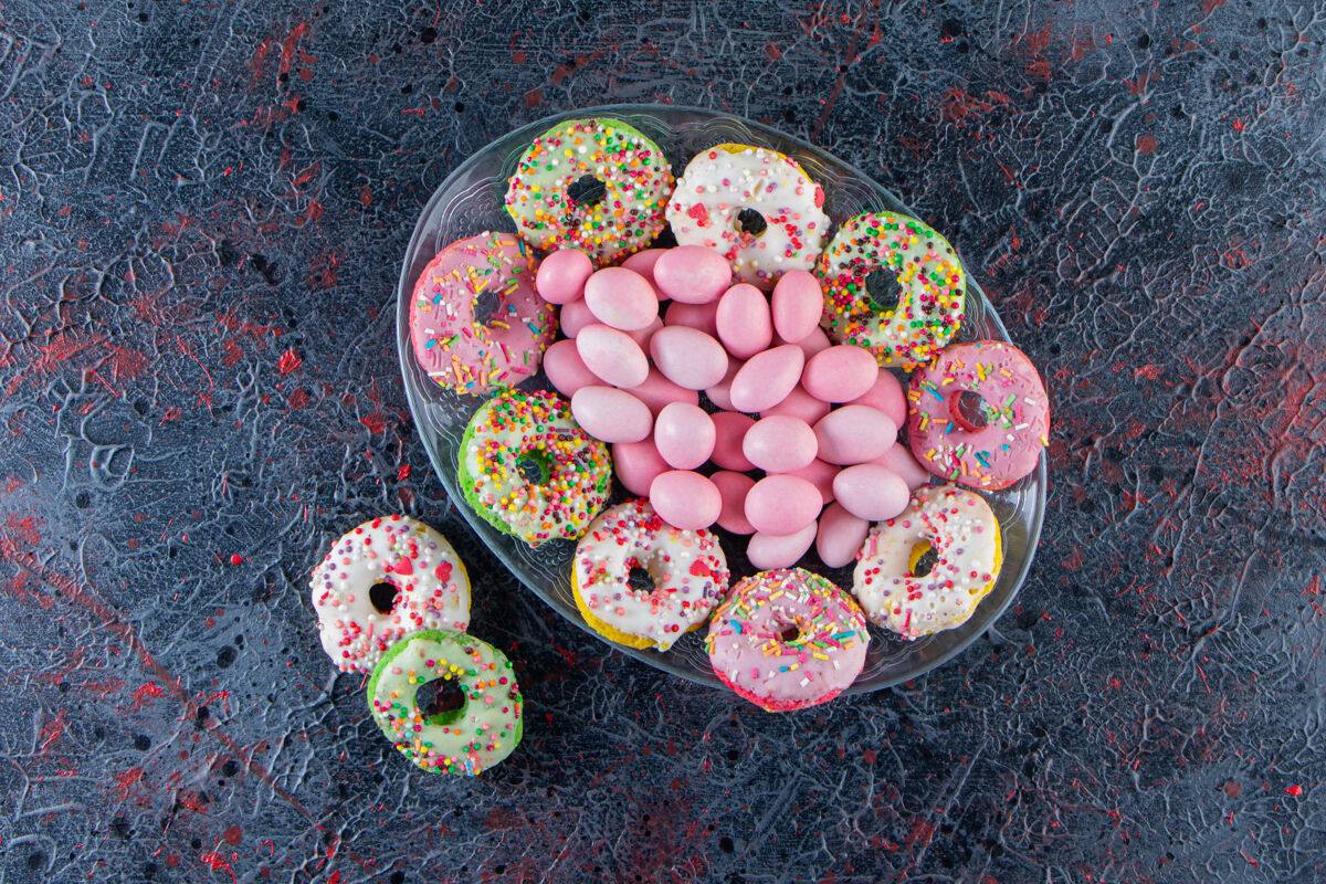 釉面在黑暗的表面上放着五颜六色的美味甜甜圈和粉红色的糖果美味面包房霜