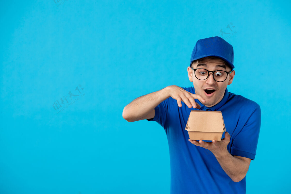 食物身穿蓝色制服的男快递员的正面图 蓝色上有小食品包服务男信使工作