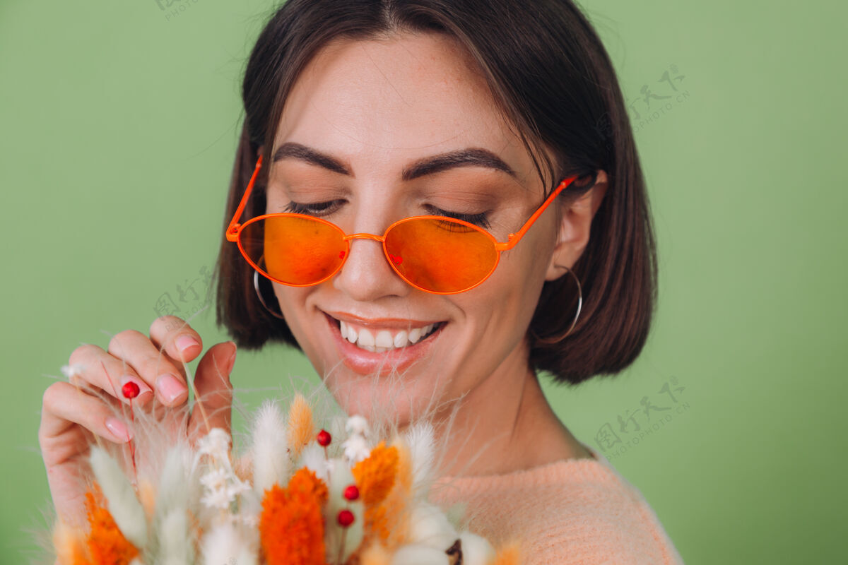 圆形年轻女子穿着休闲的桃色毛衣隔离在绿橄榄墙上捧着橘白色的花盒组成的棉花 团花 小麦和紫罗兰为礼物开心惊喜3月8日圆形盒女性