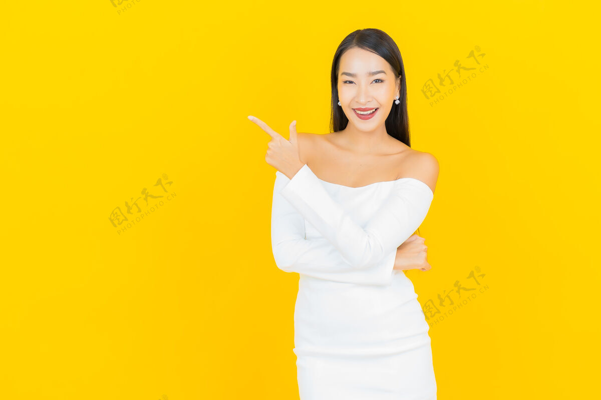 年轻美丽的亚洲年轻商业女性在黄色墙壁上穿着白色裙子微笑的画像事业西装微笑