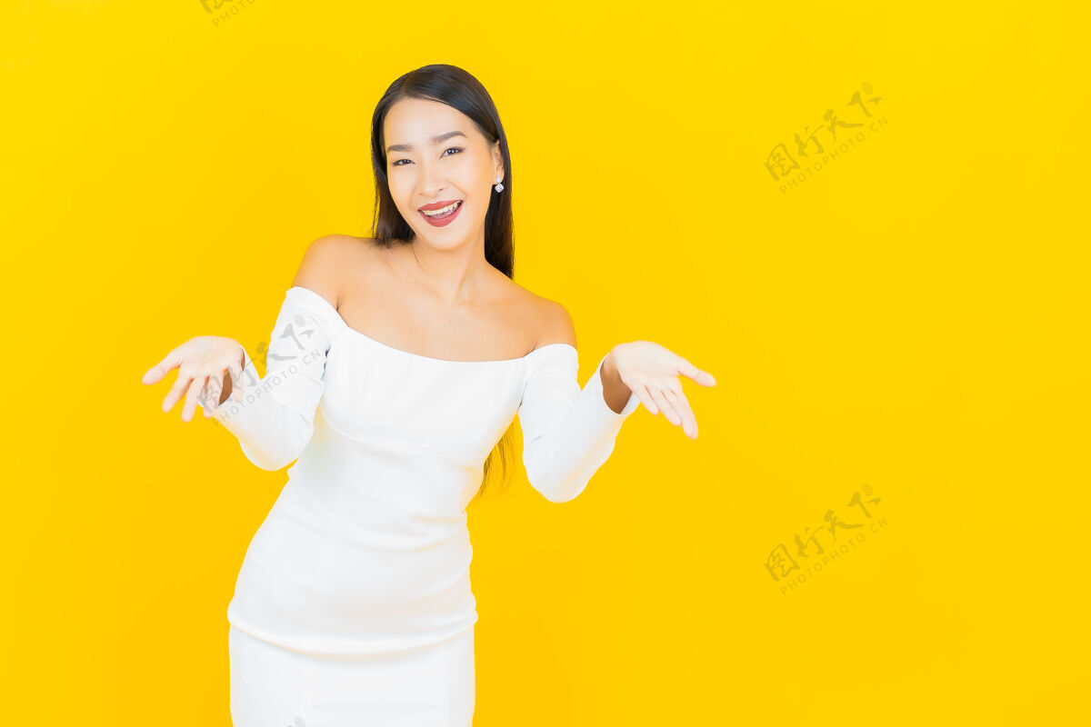 成人美丽的亚洲年轻商业女性在黄色墙壁上穿着白色裙子微笑的画像事业成功年轻
