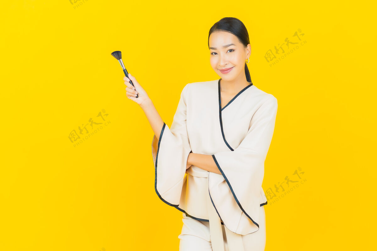 脸美丽的亚洲商界年轻女性的画像 黄色墙上有化妆刷社交时尚评论