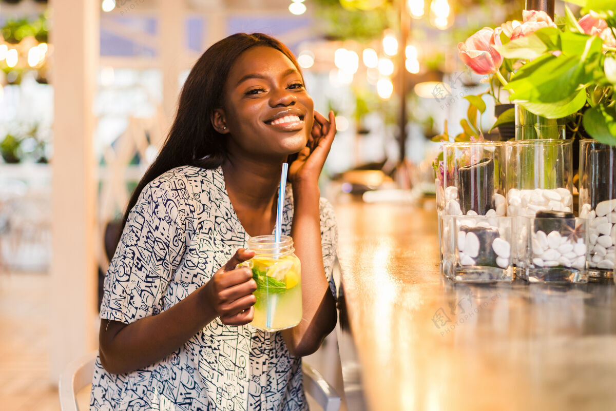 食谱快乐的非洲裔美国妇女在咖啡厅喝一杯天然柠檬水排毒饮料柠檬美味玻璃