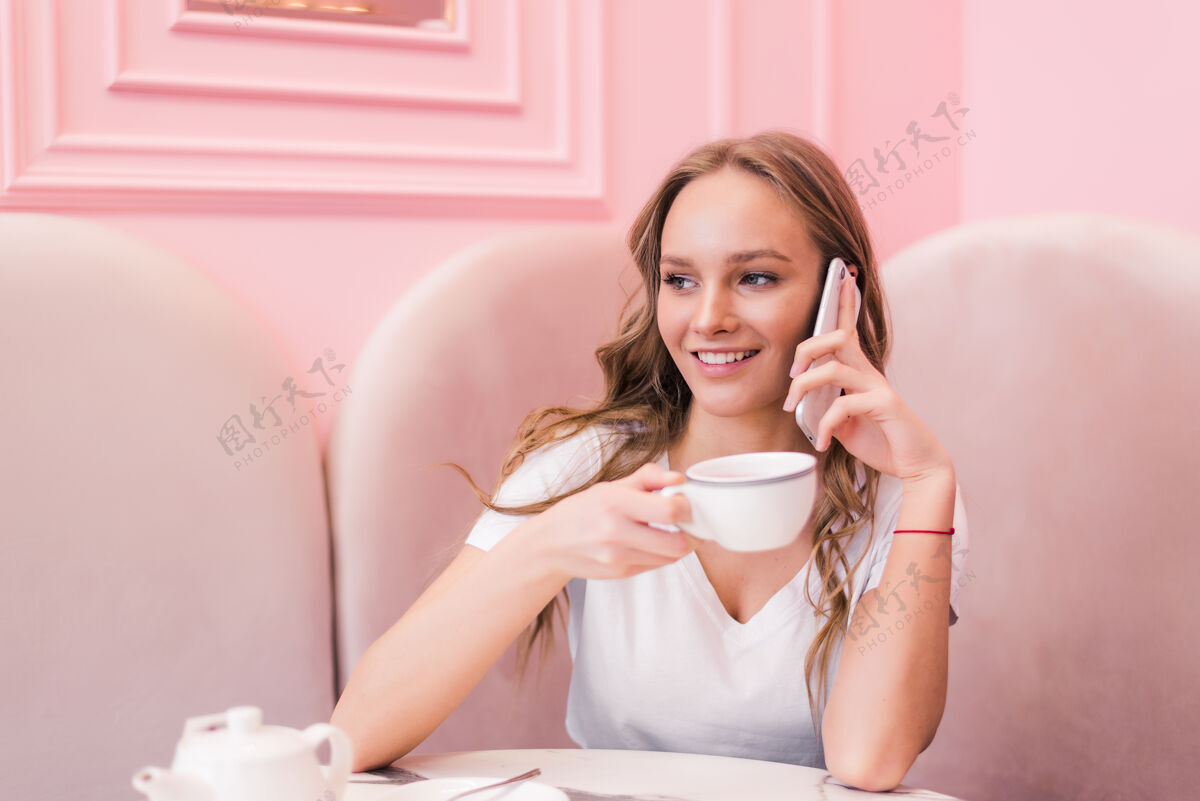 休闲一个穿着灰色衣服的年轻女子坐在咖啡馆的桌子旁 一边用手机聊天 一边在笔记本上记笔记女人桌子成人