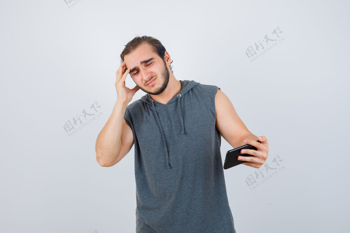 手指一个穿着连帽t恤的年轻人看着电话 手指放在头上 看起来很沮丧 正面视图成人悲伤不高兴