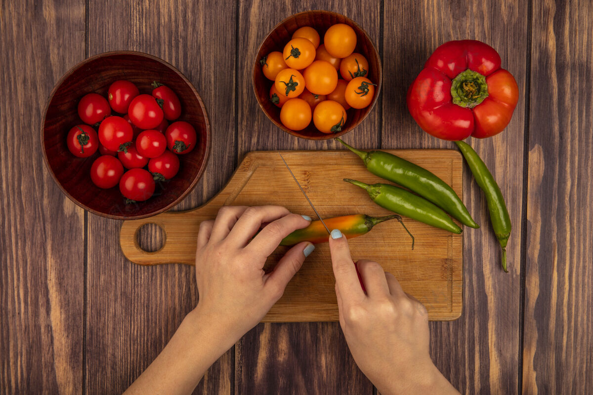 膳食俯视图中的女性手切一个新鲜的胡椒在一个木制的厨房板与樱桃西红柿刀在一个木制的碗在一个木制的表面厨房樱桃美味